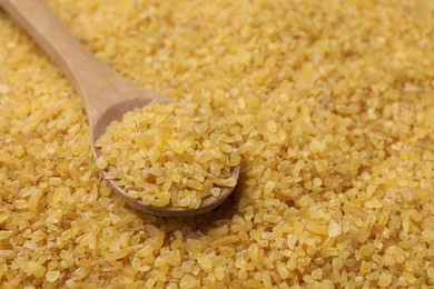 Photo of Wooden spoon on raw bulgur, closeup. Space for text
