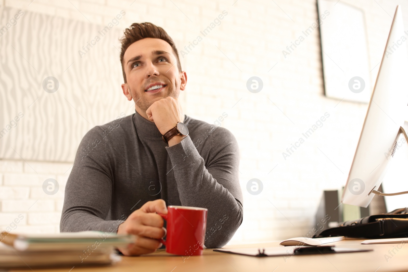 Photo of Young man with cup of drink relaxing at table in office during break