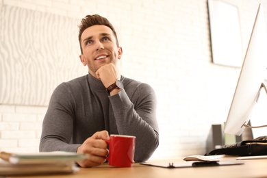 Young man with cup of drink relaxing at table in office during break