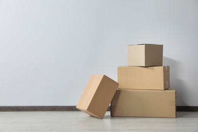 Photo of Many closed cardboard boxes on floor near white wall, space for text. Delivery service