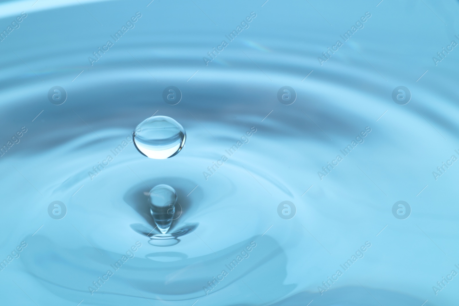 Photo of Drop falling into clear water on light blue background, closeup