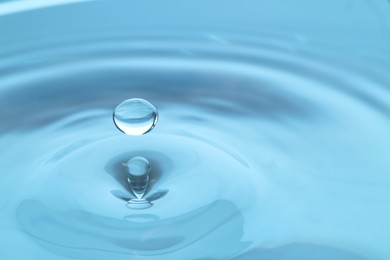 Photo of Drop falling into clear water on light blue background, closeup