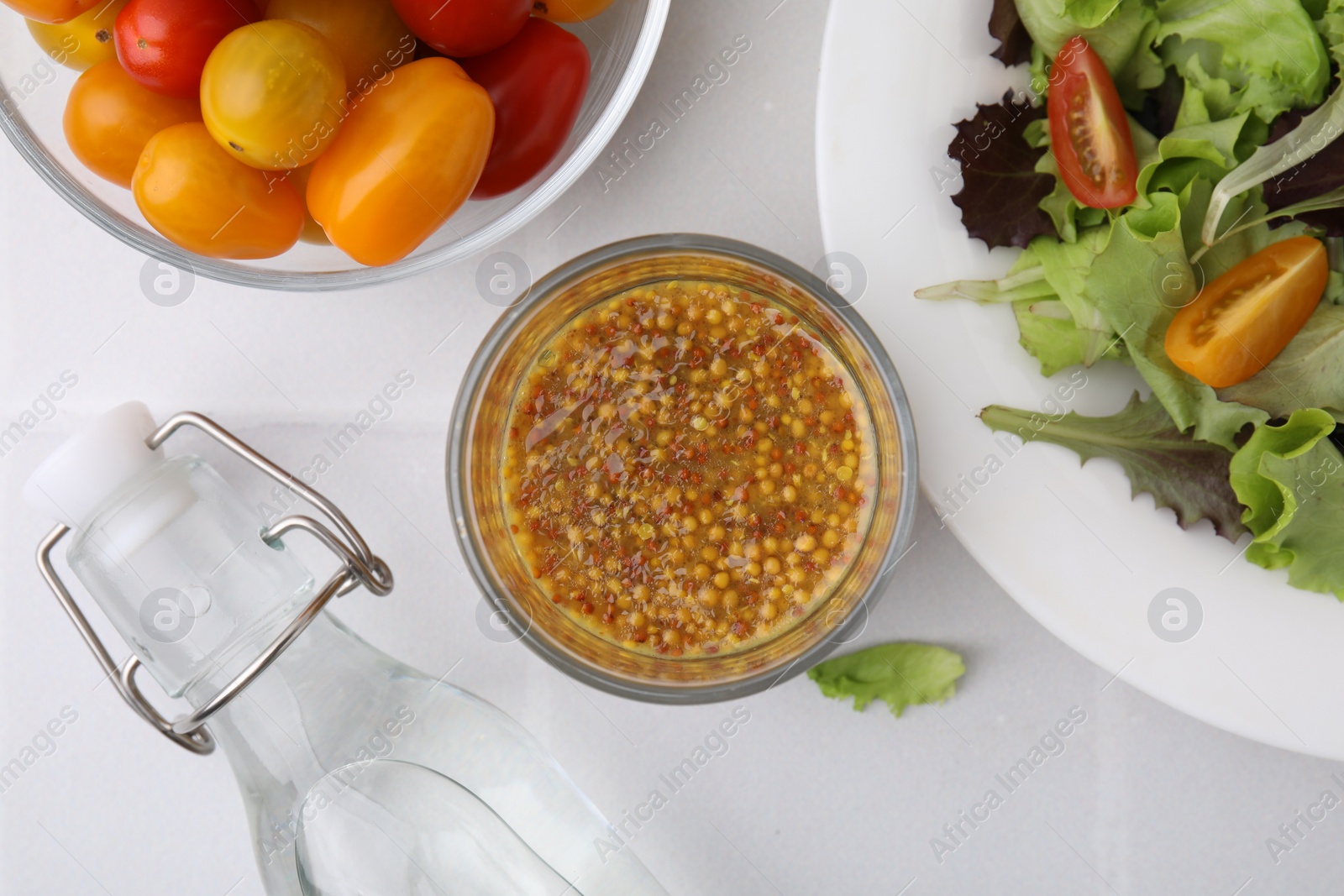 Photo of Tasty vinaigrette sauce in glass, vinegar, tomatoes and salad on light tiled table, flat lay