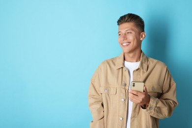 Happy young man sending message via smartphone on light blue background. Space for text