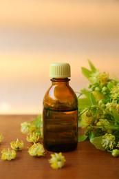 Photo of Bottle of essential oil and linden blossoms on wooden table against blurred background