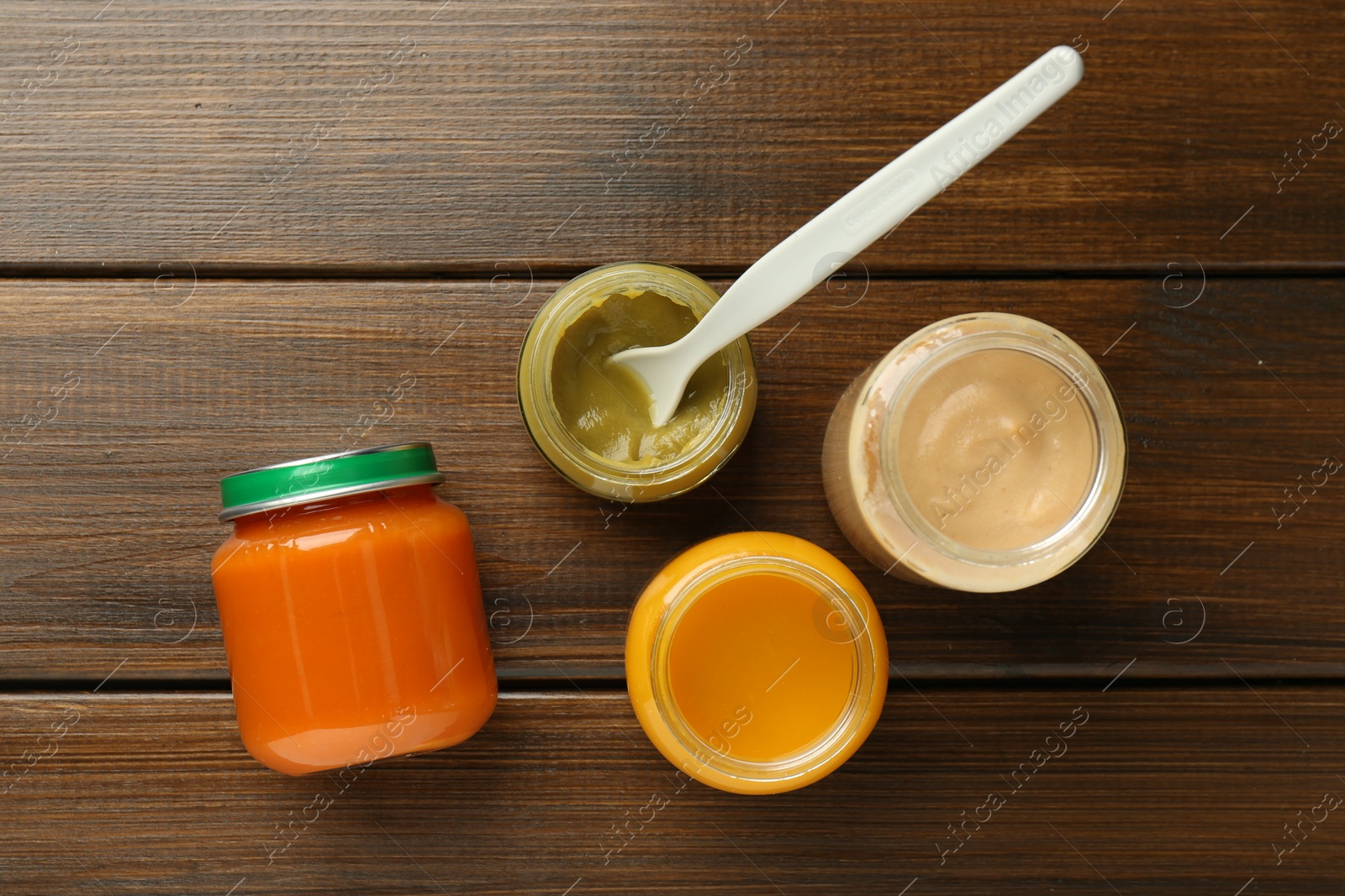 Photo of Tasty baby food in jars on wooden table, flat lay