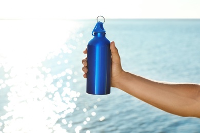 Photo of Young sporty man holding water bottle near river on sunny day. Space for text