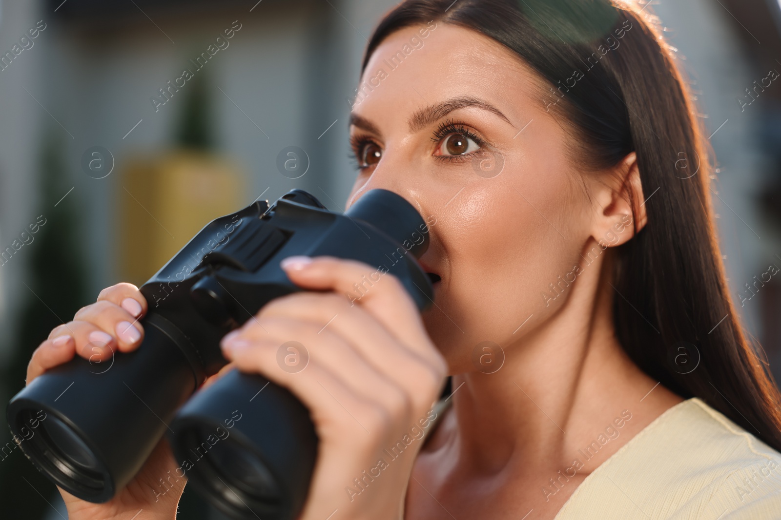 Photo of Concept of private life. Curious young woman with binoculars spying on neighbours outdoors, closeup