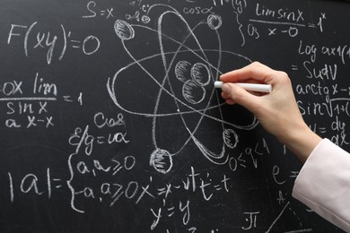 Photo of Teacher writing physical formulas with chalk on black chalkboard, closeup