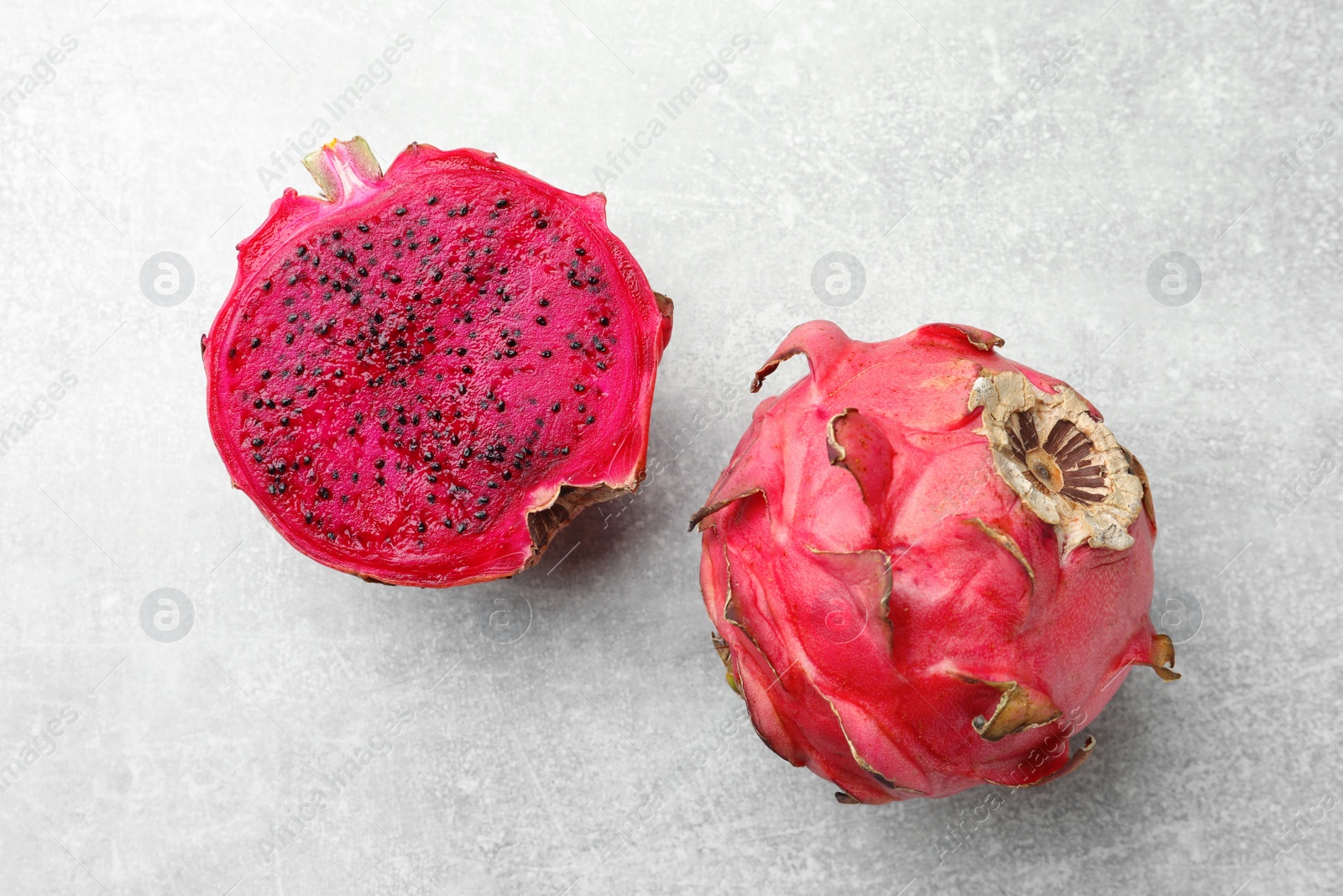 Photo of Delicious cut and whole red pitahaya fruits on light grey table, flat lay