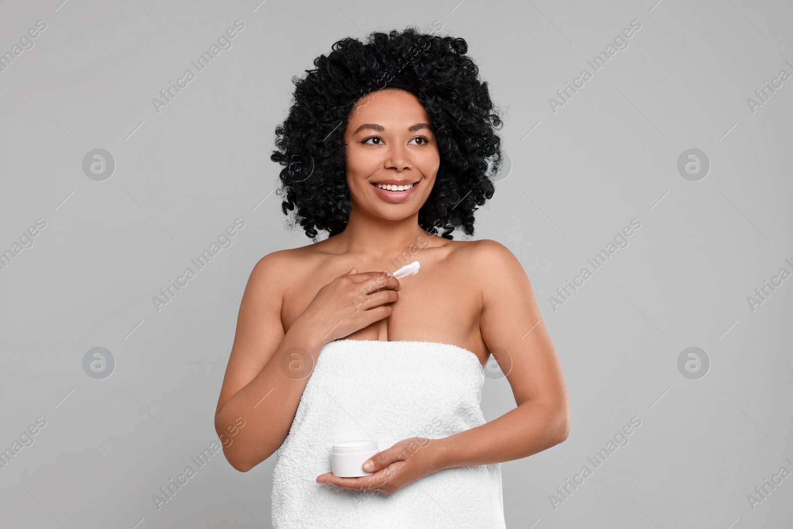 Photo of Young woman applying cream onto body on grey background