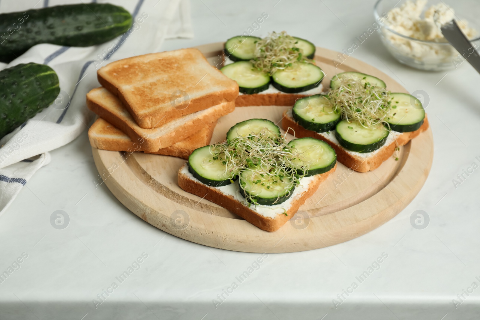 Photo of Tasty toasts with cucumber, cream cheese and microgreens on white table