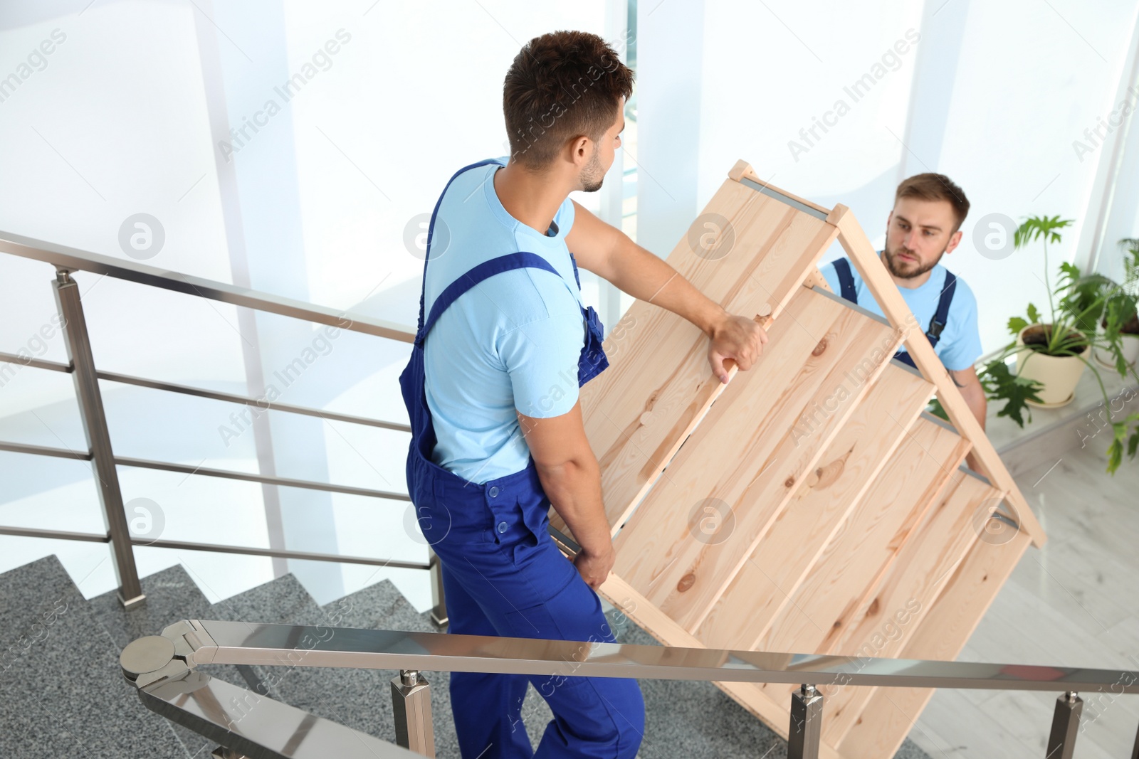 Photo of Professional workers carrying wooden rack on stairs in office. Moving service
