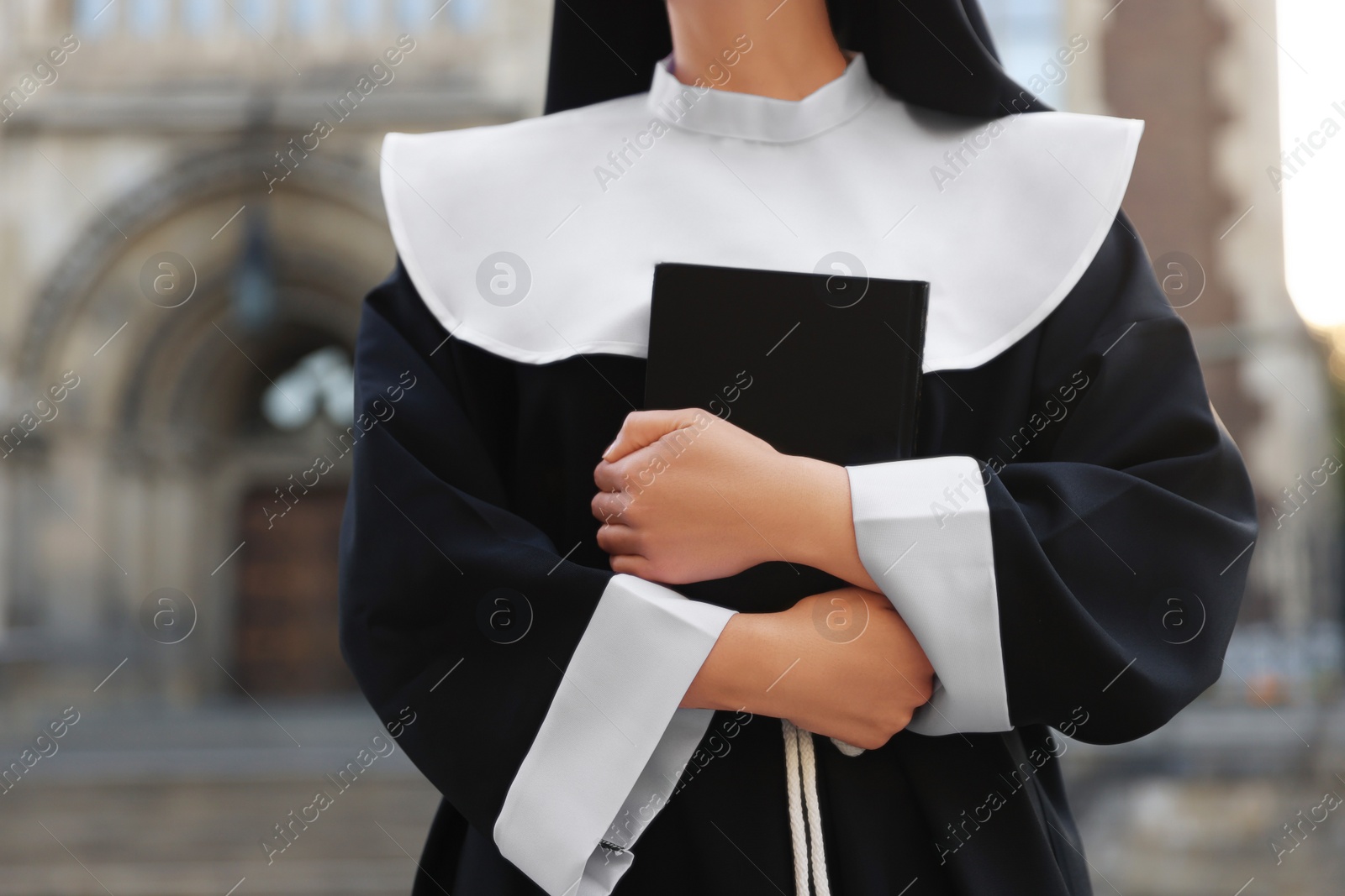 Photo of Young nun with Bible near building outdoors, closeup