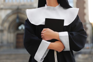 Young nun with Bible near building outdoors, closeup
