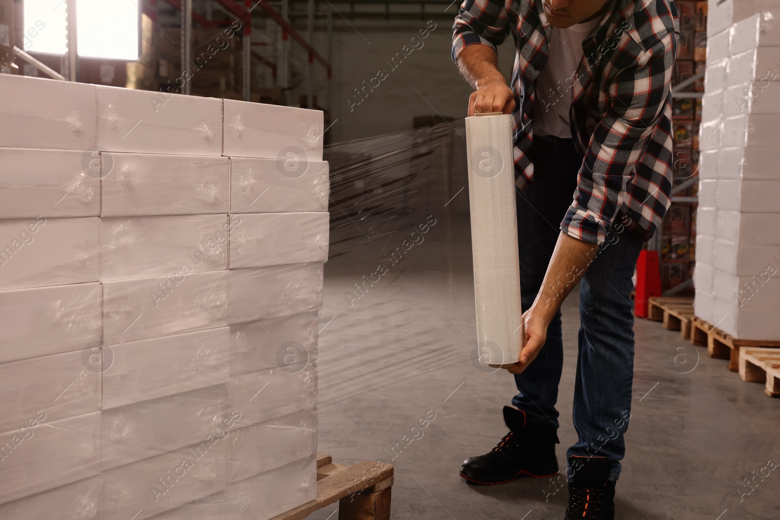 Photo of Worker wrapping boxes in stretch film at warehouse, closeup