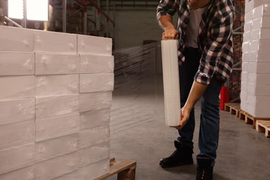 Worker wrapping boxes in stretch film at warehouse, closeup