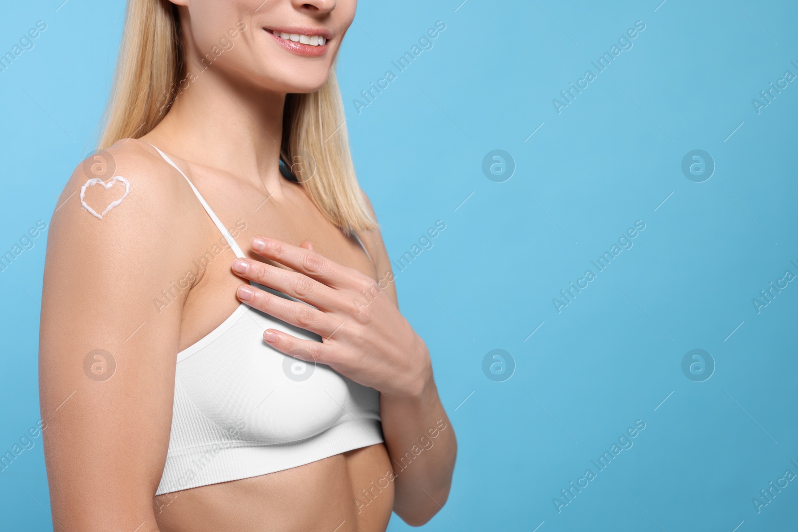 Photo of Woman with body cream onto her arm against light blue background, closeup. Space for text