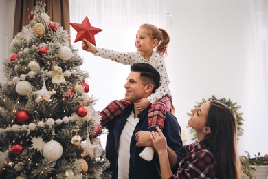 Family decorating Christmas tree with star topper indoors