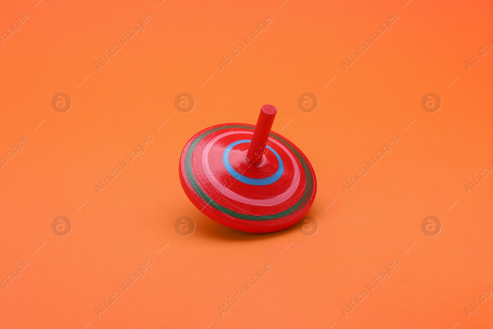 Photo of One bright spinning top on orange background. Toy whirligig