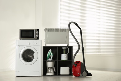 Photo of Modern vacuum cleaner and different household appliances near window indoors