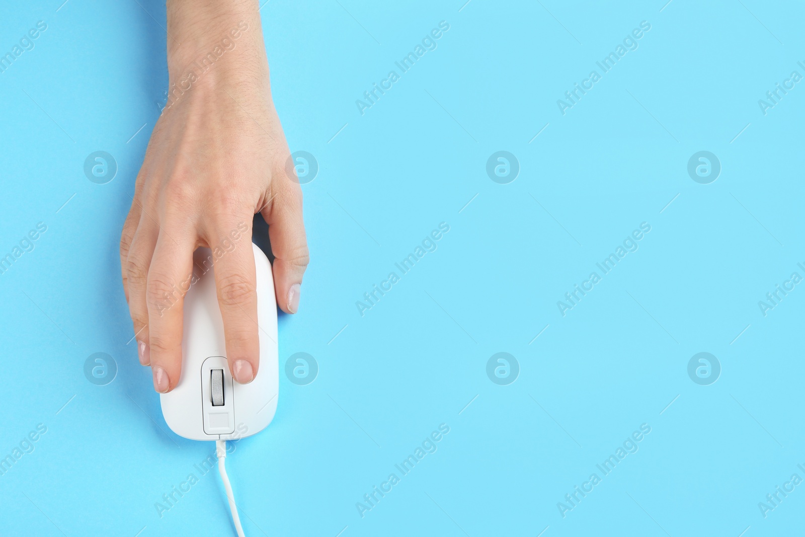 Photo of Woman using modern wired optical mouse on light blue background, top view. Space for text