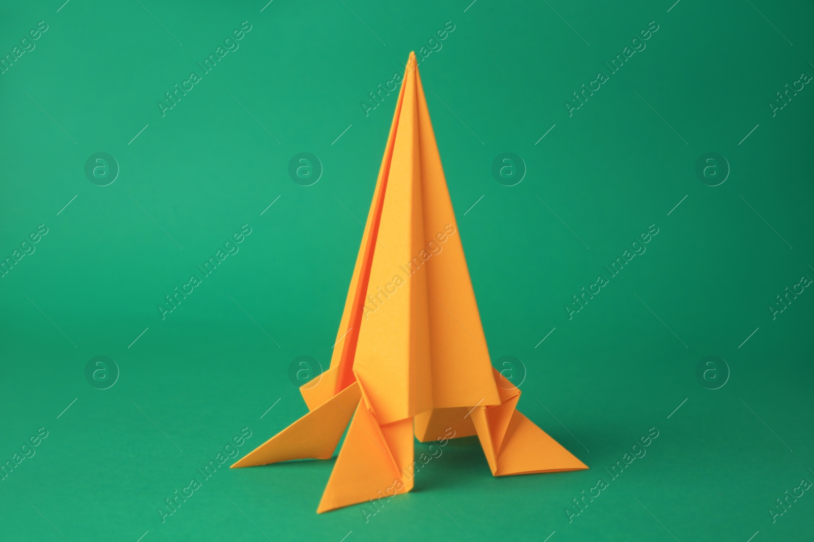 Photo of Origami art. Handmade yellow paper rocket on green background