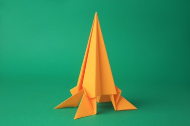 Photo of Origami art. Handmade yellow paper rocket on green background