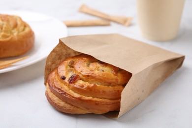 Photo of Delicious roll with raisins in paper bag on white table, closeup. Sweet bun