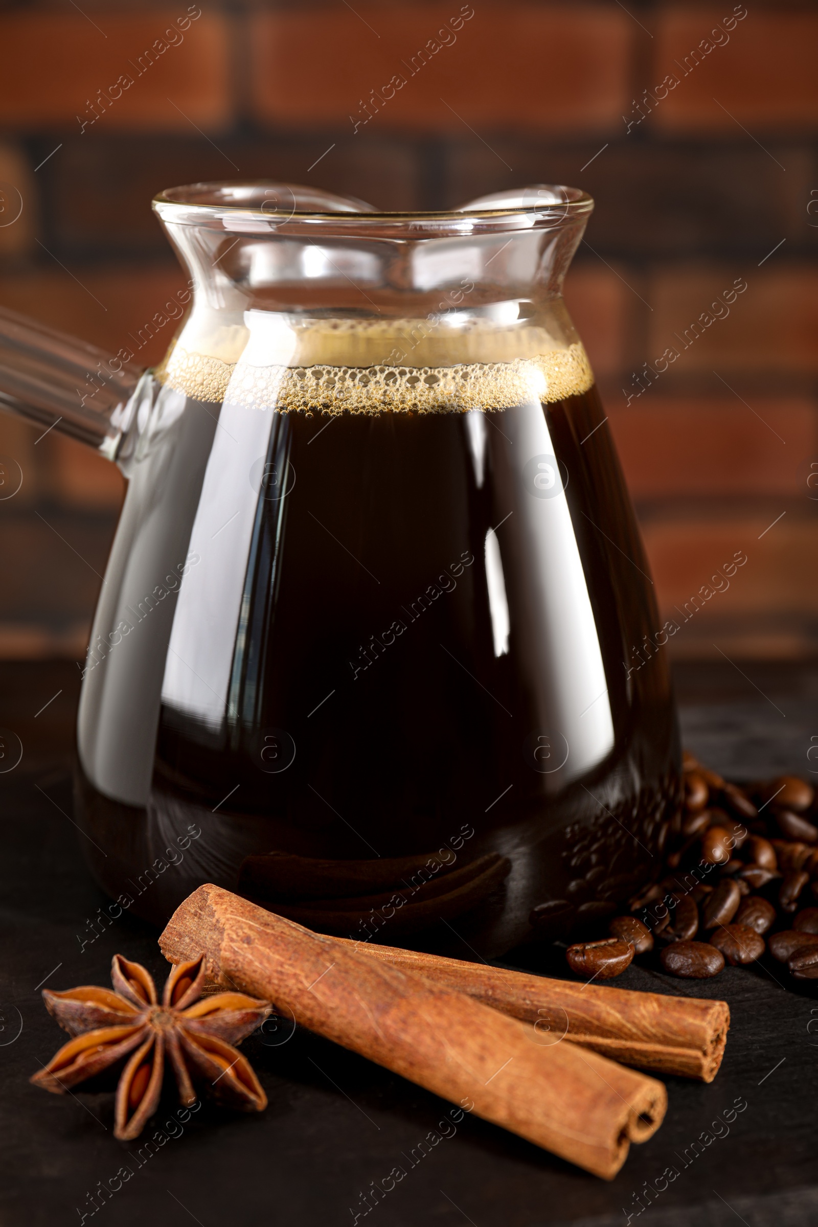 Photo of Glass turkish coffee pot with hot drink, cinnamon sticks and anise star on wooden table