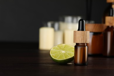 Bottle of essential oil and lime on wooden table, space for text