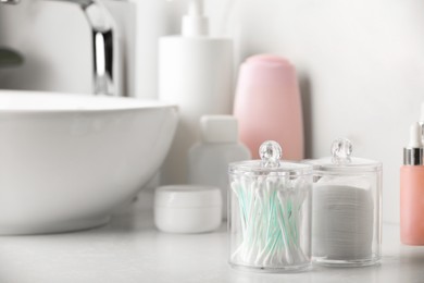 Photo of Containers with cotton swabs and pads near cosmetic products on white countertop in bathroom. Space for text