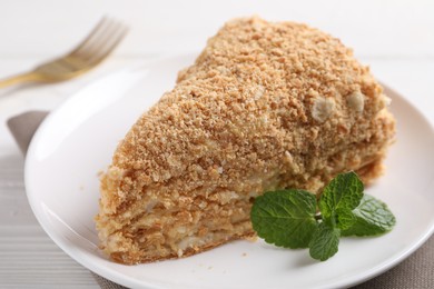 Piece of delicious Napoleon cake with mint on table, closeup