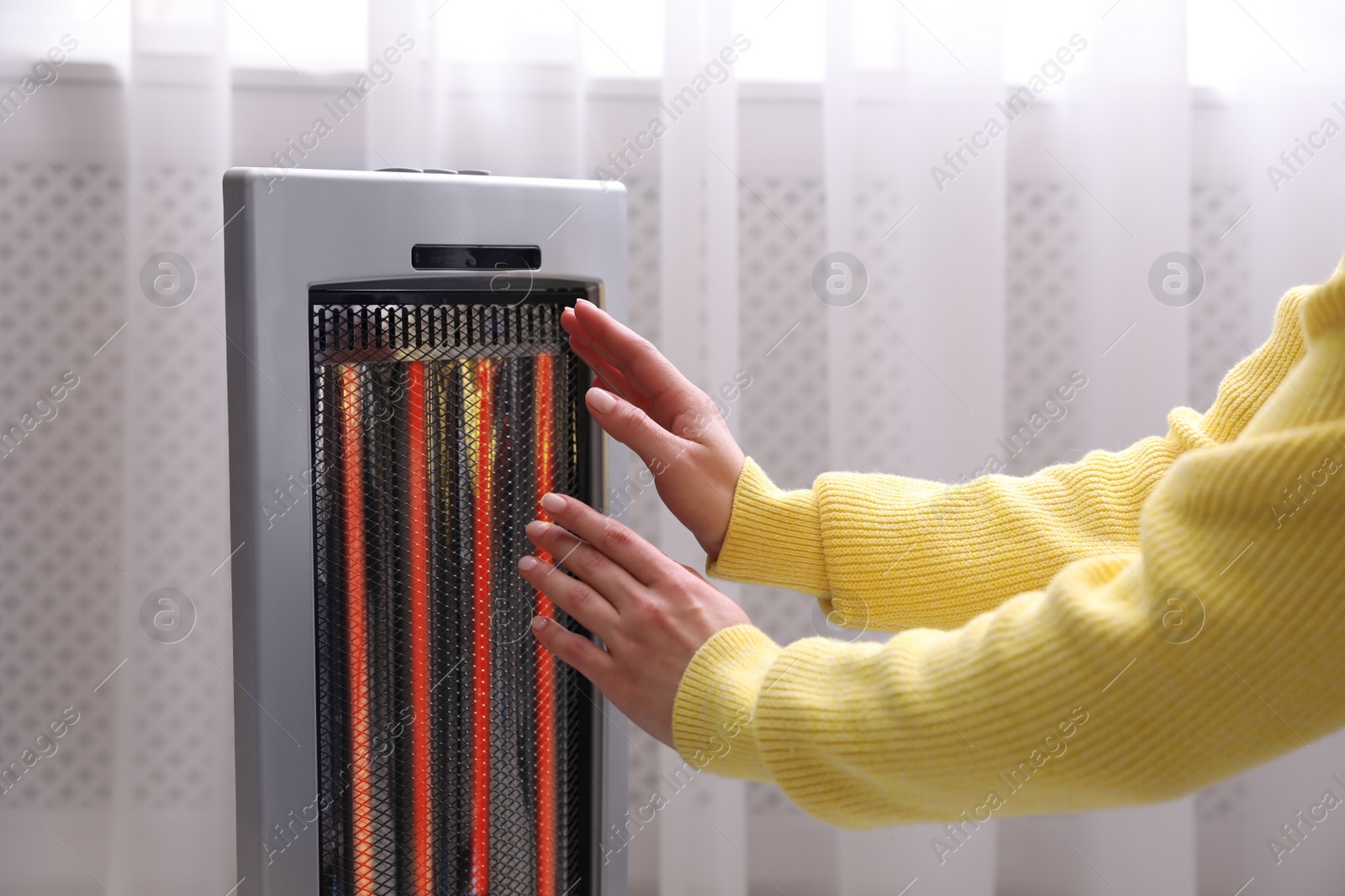 Photo of Woman warming hands near heater indoors, closeup