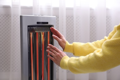 Woman warming hands near heater indoors, closeup