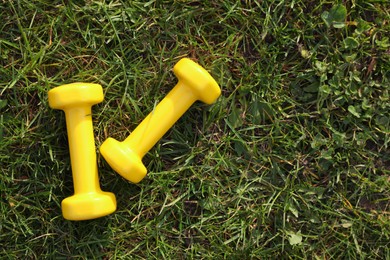 Yellow dumbbells on green grass, top view with space for text. Morning exercise