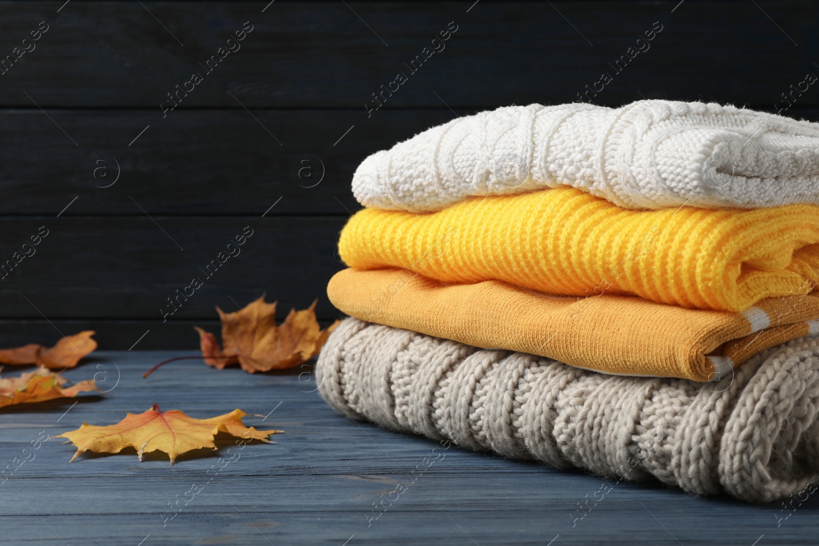 Photo of Stack of folded knitted sweaters and autumn leaves on table. Space for text