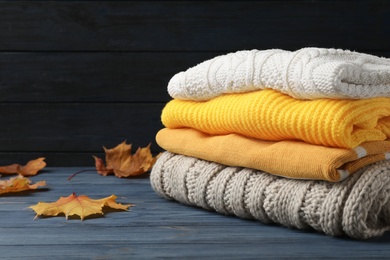 Photo of Stack of folded knitted sweaters and autumn leaves on table. Space for text