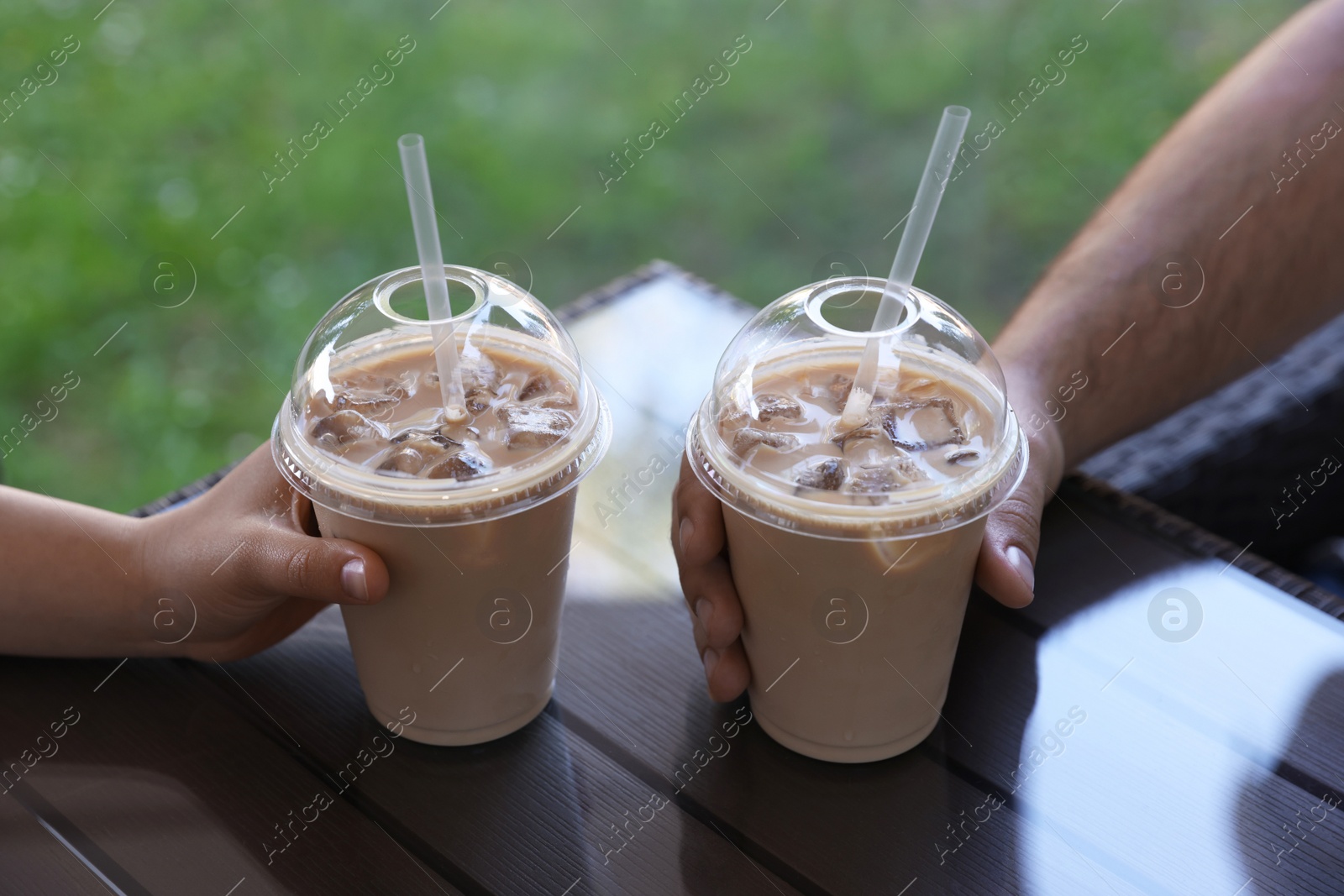 Photo of Man and woman with plastic takeaway cups of delicious iced coffee at table in outdoor cafe, closeup