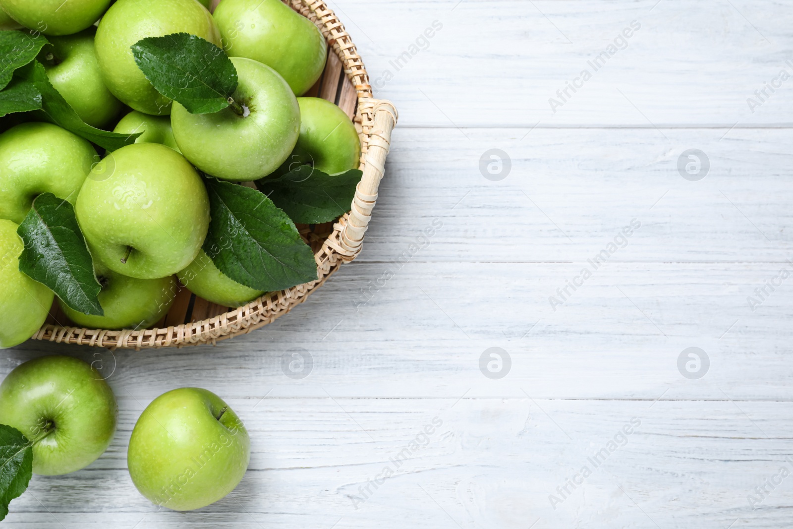 Photo of Juicy green apples in wicker tray on white wooden table, flat lay. Space for text