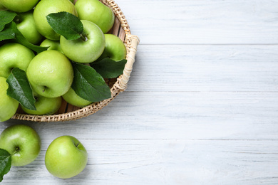 Photo of Juicy green apples in wicker tray on white wooden table, flat lay. Space for text