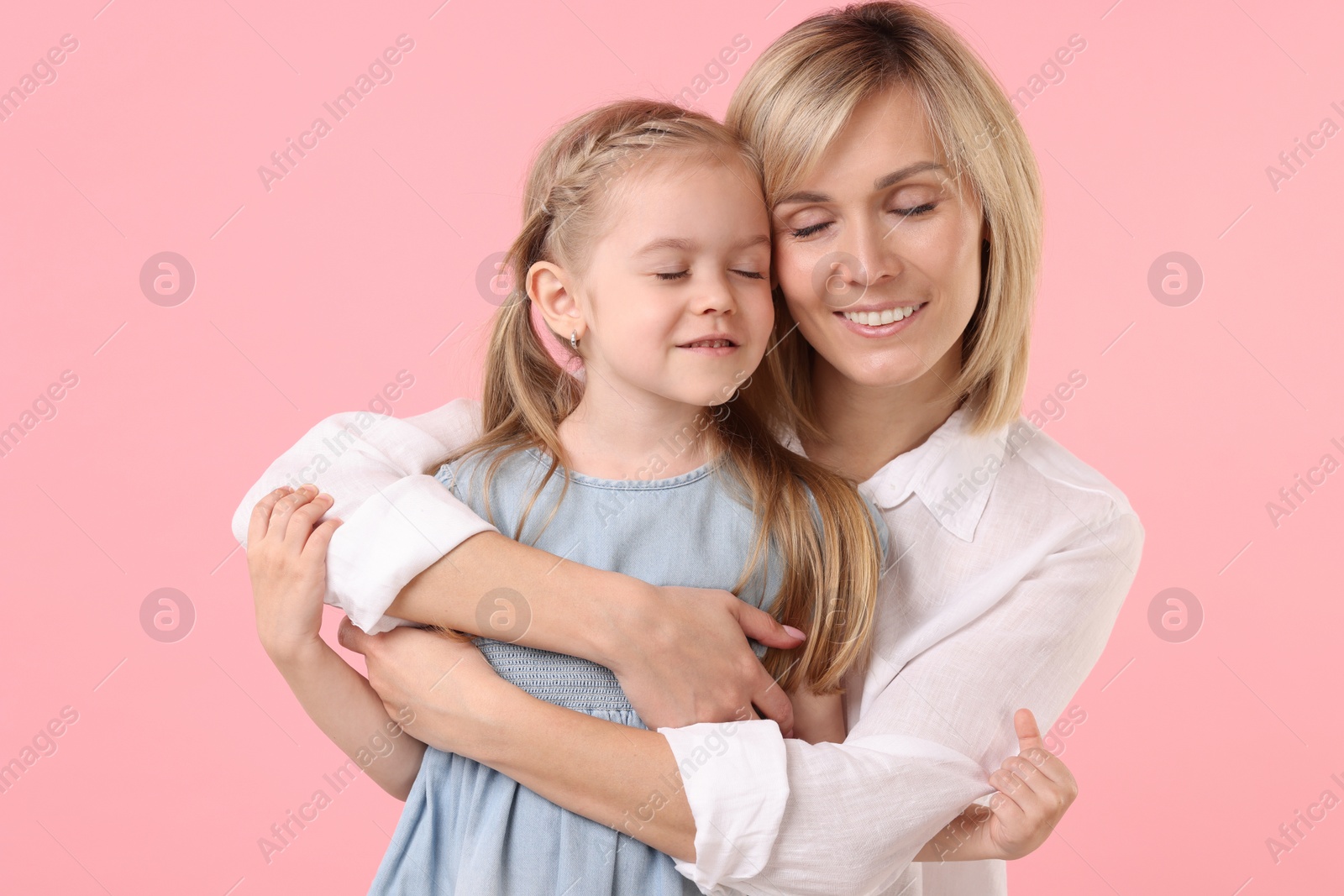 Photo of Mother hugging her happy daughter on pink background