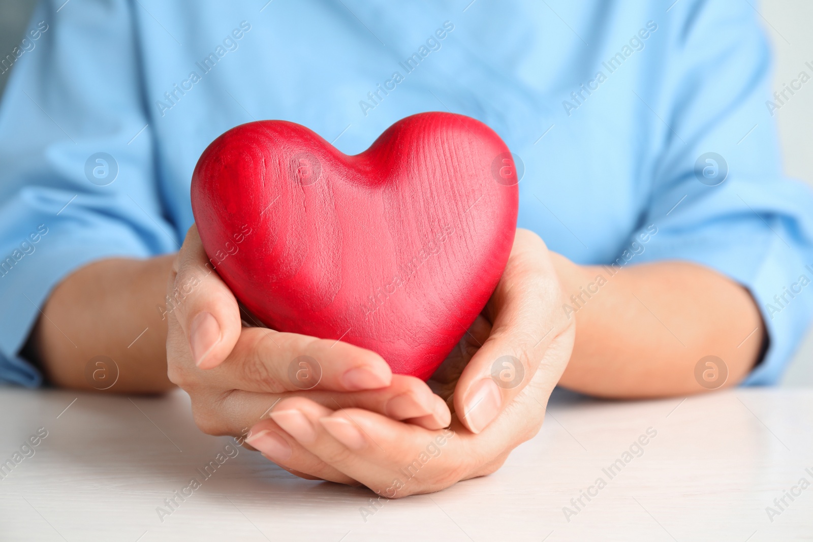 Photo of Doctor holding red heart at wooden table, closeup. Cardiology concept