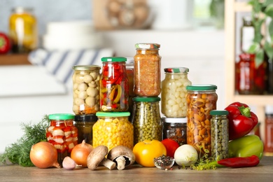 Fresh vegetables and jars of pickled products on wooden table
