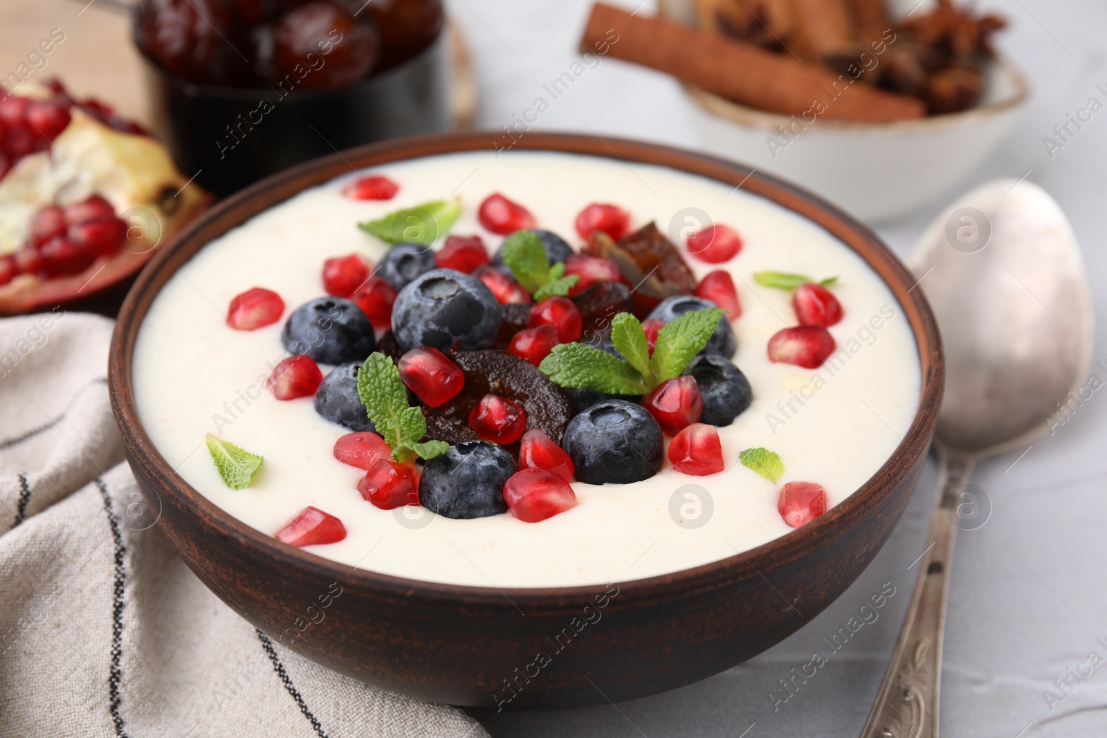 Photo of Delicious semolina pudding with blueberries, pomegranate, dates and mint in bowl on white table, closeup