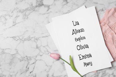 List of baby names, tulip flower and child's clothes on white marble background, flat lay. Space for text