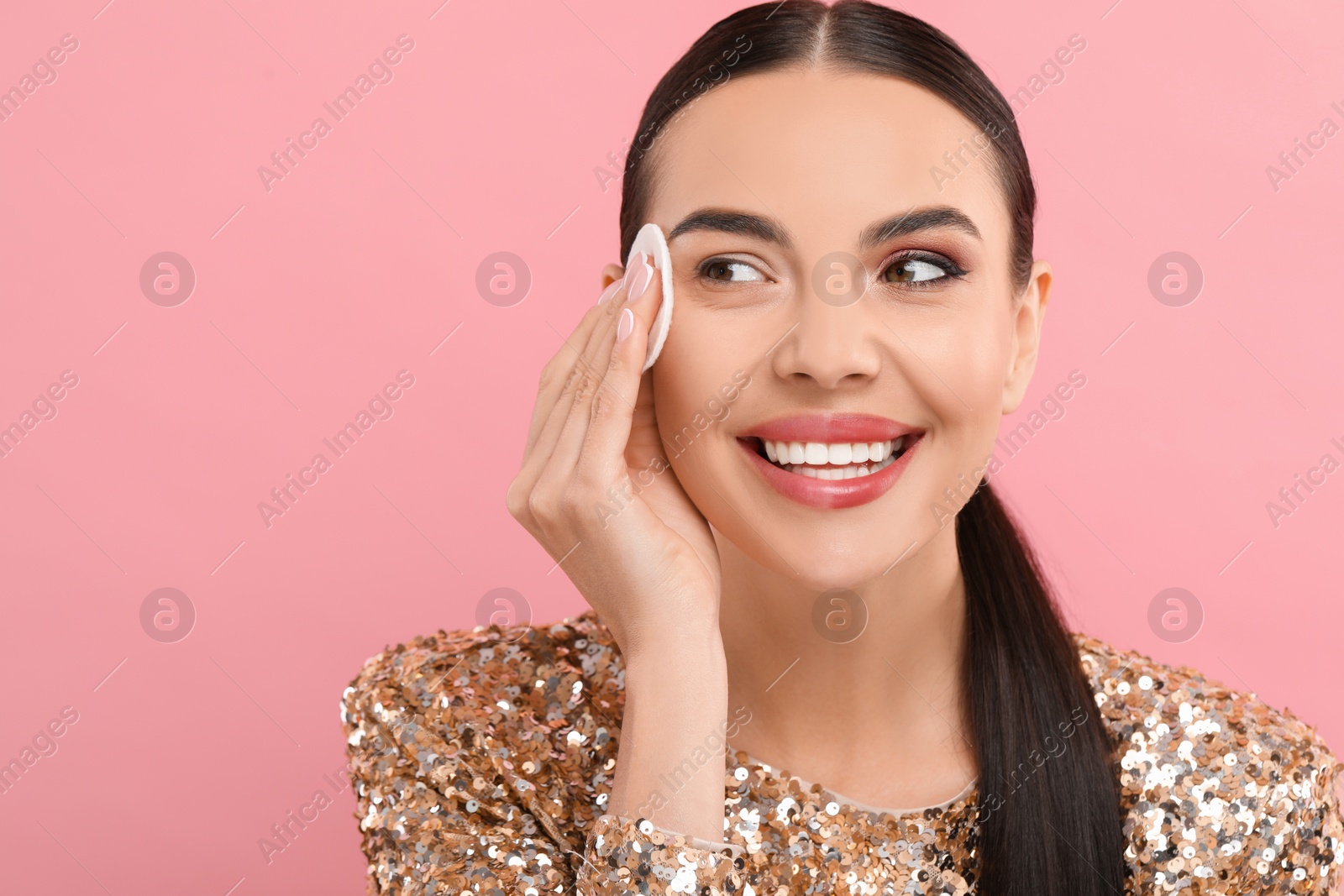 Photo of Beautiful woman removing makeup with cotton pad on pink background. Space for text