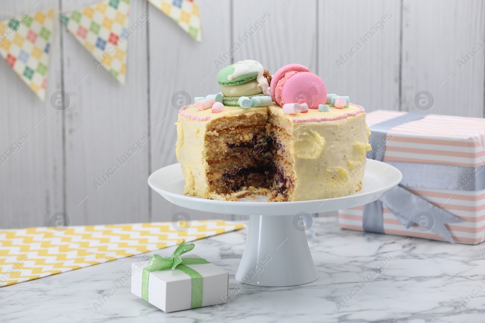 Photo of Delicious cake decorated with macarons and marshmallows and gift boxes on white marble table