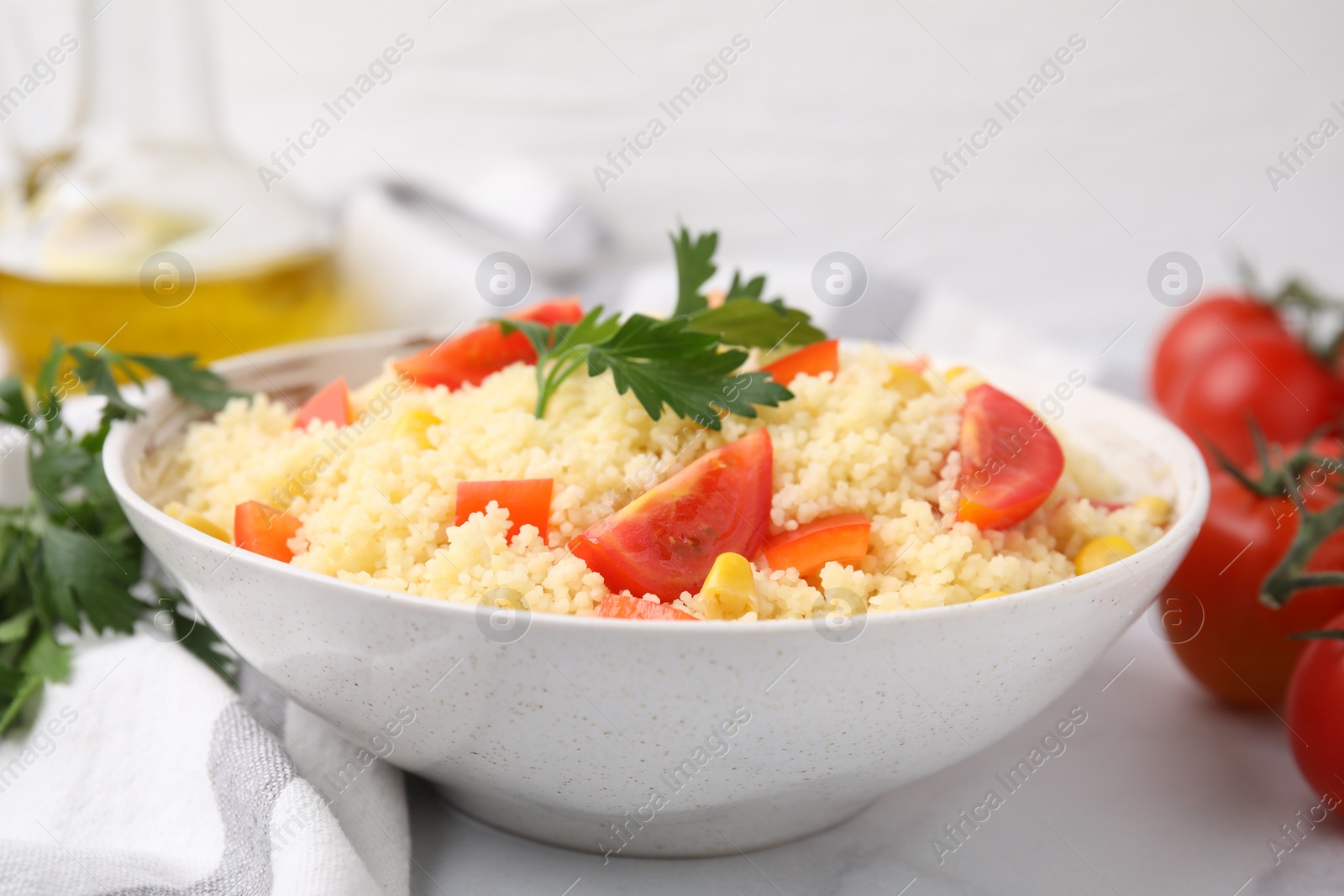 Photo of Tasty couscous with parsley, corn and tomatoes in bowl on white table, closeup