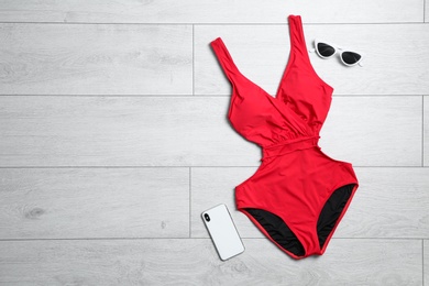 Photo of One-piece swimsuit, sunglasses and smartphone on wooden background